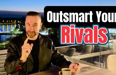 Andy Holt wearing a black leather jacket, seated on an outdoor terrace in Krakow, Poland at night with a river and lit-up bridge in the background. Overlaid text reads “Outsmart Your Rivals.”